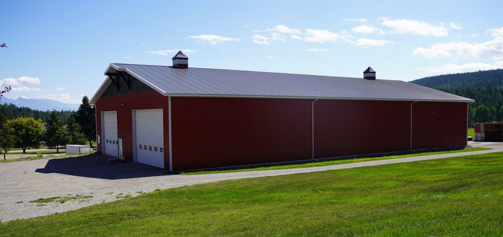A dark red post-frame agriculture storage building with cupolas