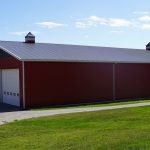A dark red post-frame agriculture storage building with cupolas