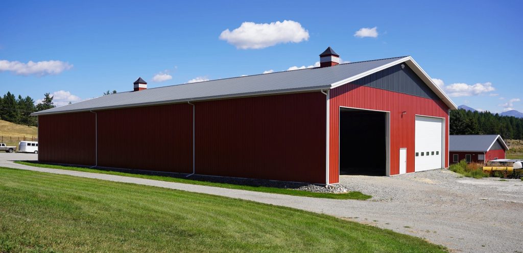A dark red post-frame agriculture storage building with cupolas