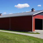 A dark red post-frame agriculture storage building with cupolas