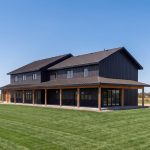 A charcoal residential post-frame Farmhouse with wainscoting, and a wrap around porch