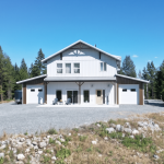 A custom white white post-frame Barndominium with timber accents, and a front porch