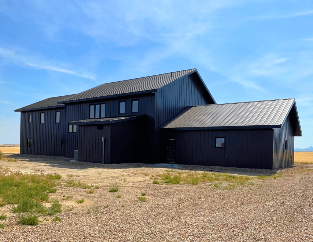 A charcoal residential post-frame Farmhouse with wainscoting, and a wrap around porch