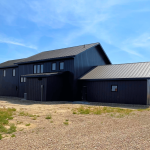 A charcoal residential post-frame Farmhouse with wainscoting, and a wrap around porch