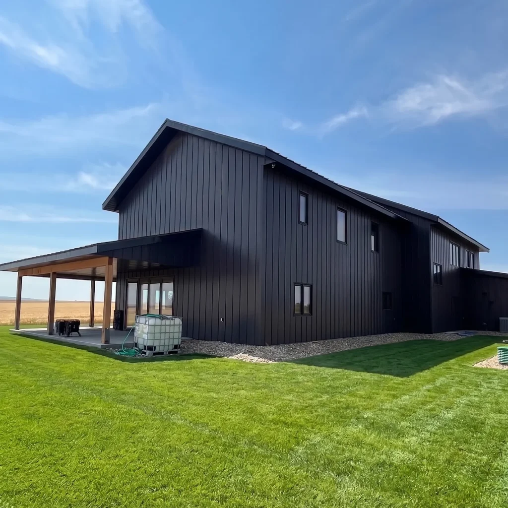 A charcoal residential post-frame Farmhouse with wainscoting, and a wrap around porch