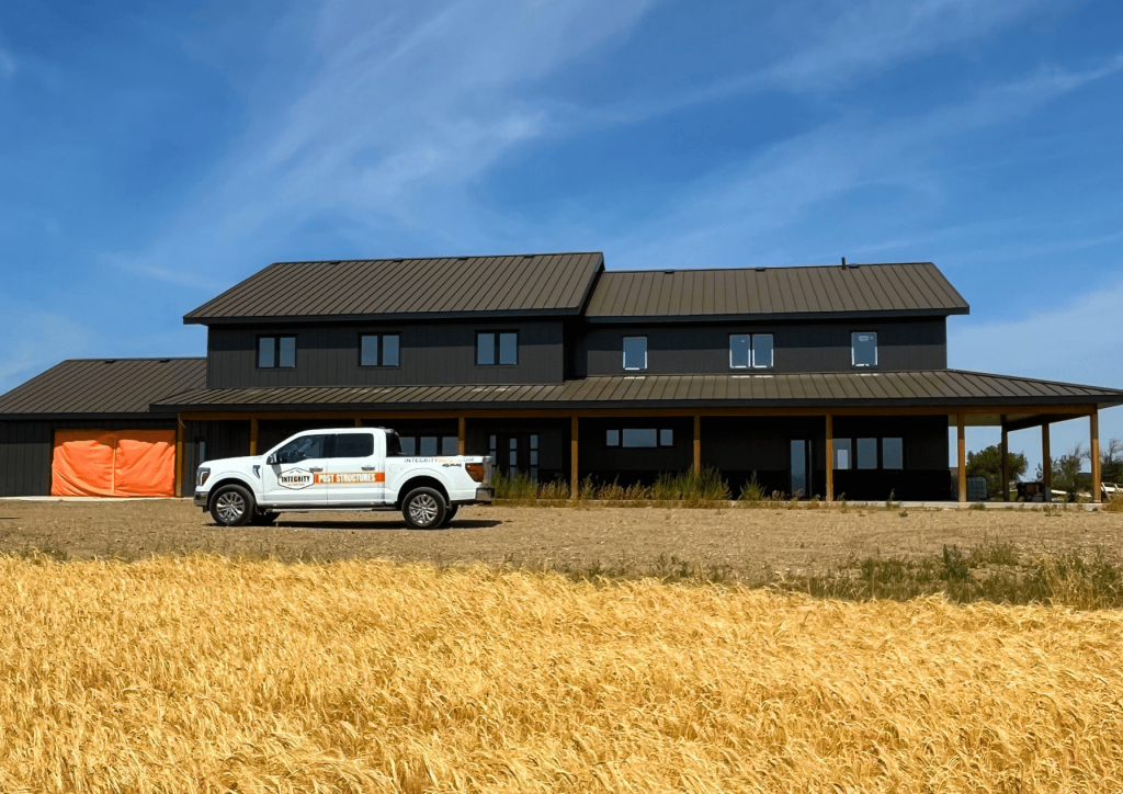 A charcoal residential post-frame Farmhouse with wainscoting, and a wrap around porch