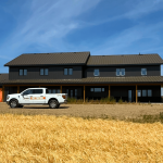 A charcoal residential post-frame Farmhouse with wainscoting, and a wrap around porch