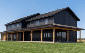 A charcoal residential post-frame Farmhouse with wainscoting, and a wrap around porch