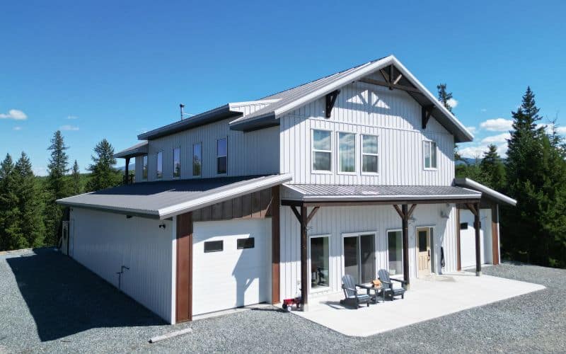 A custom white white post-frame Barndominium with timber accents, and a front porch