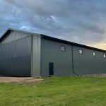 A dark sage post-frame agriculture machine shed