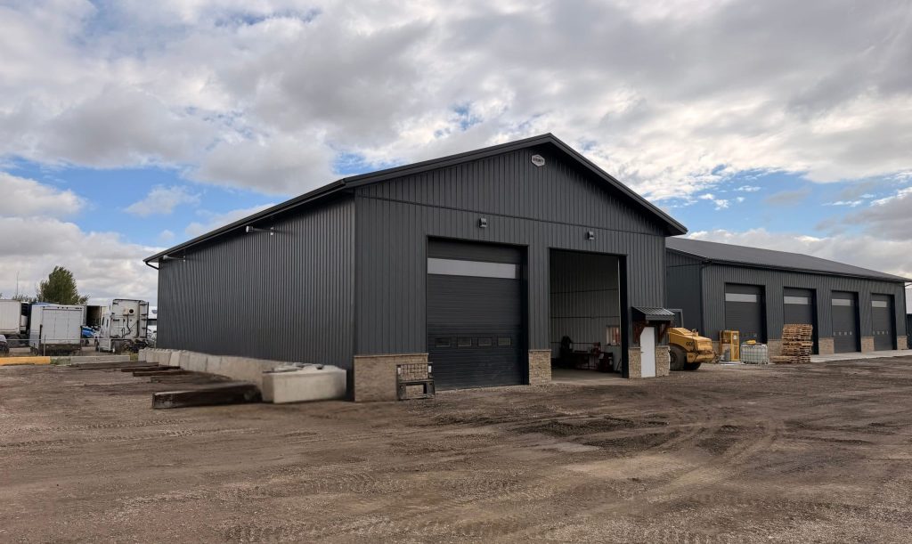 A gunmetal post-frame storage building with wainscoting, soffits, and overhead doors