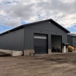 A gunmetal post-frame storage building with wainscoting, soffits, and overhead doors