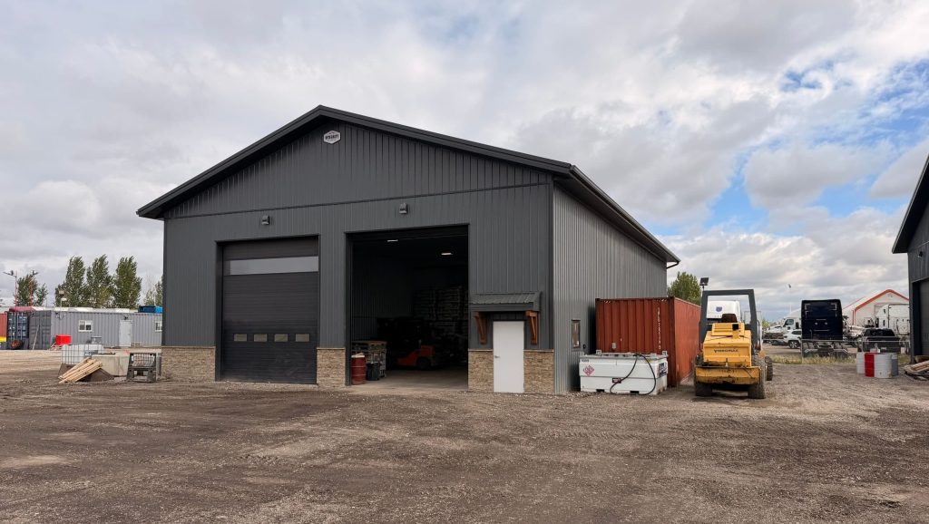 A gunmetal post-frame storage building with wainscoting, soffits, and overhead doors