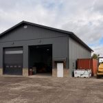A gunmetal post-frame storage building with wainscoting, soffits, and overhead doors