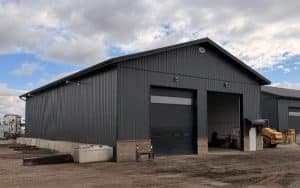 A gunmetal post-frame storage building with wainscoting, soffits, and overhead doors