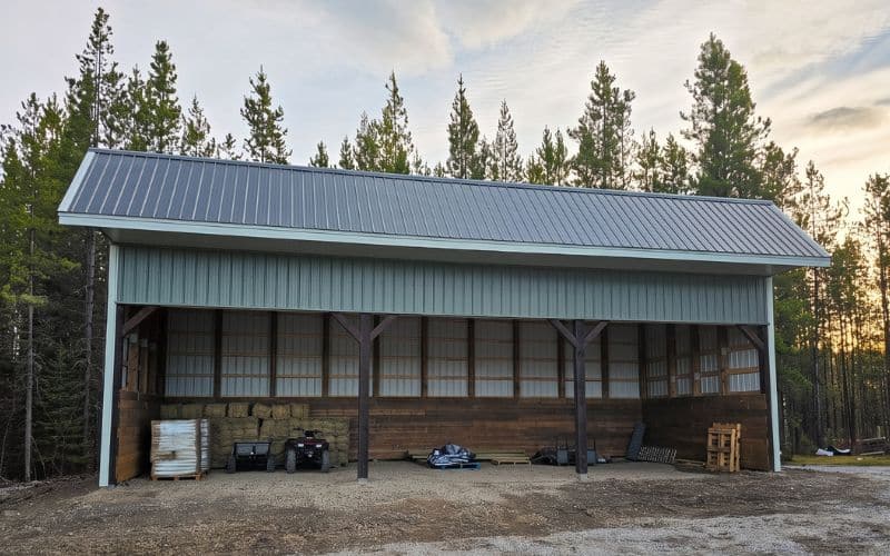 A dark sage post-frame livestock shelter with kick-wall