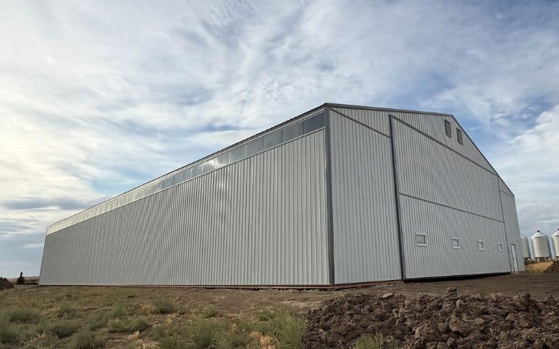 A bone white post-frame agriculture storage building with a bi-fold and wall lights