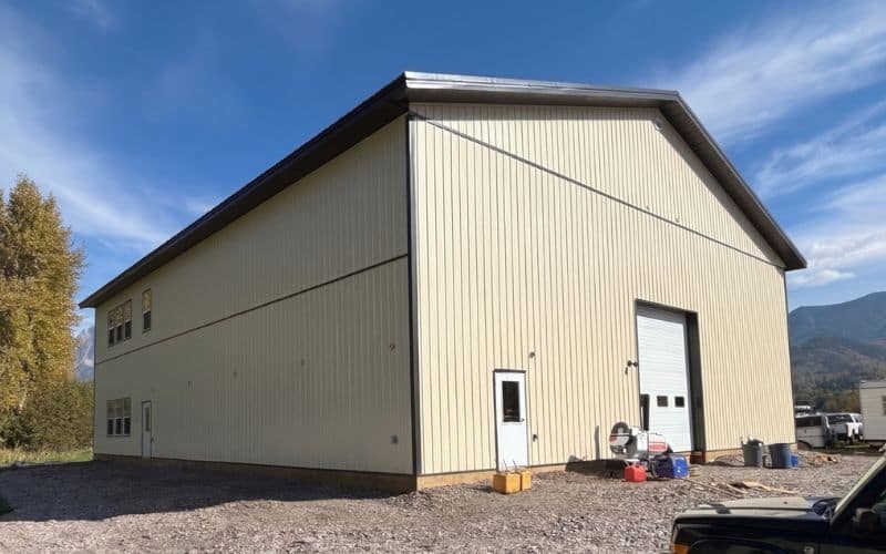 An antique linen post-frame storage building with dark brown roof and trims